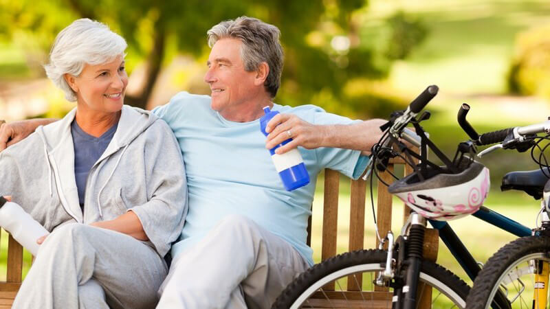 Äteres Paar entspannt auf Parkbank, daneben Fahrräder