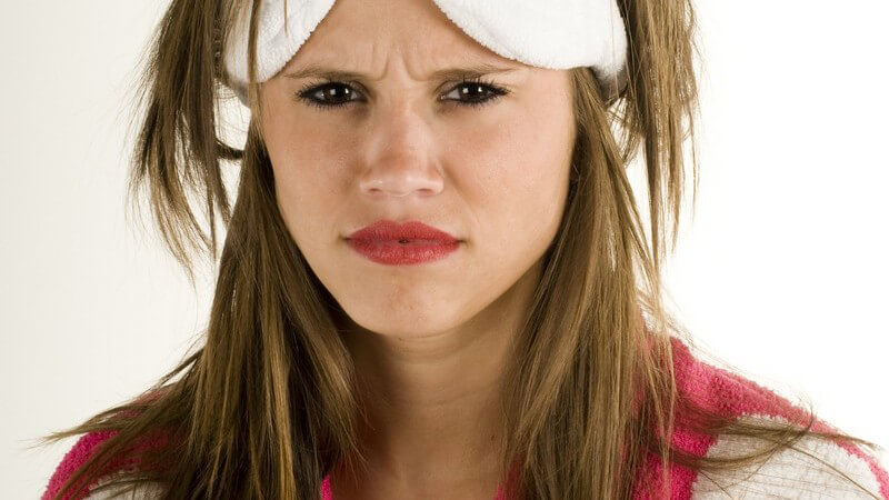 Junge Frau am Morgen in Bademantel mit Schlafmaske nicht gut drauf