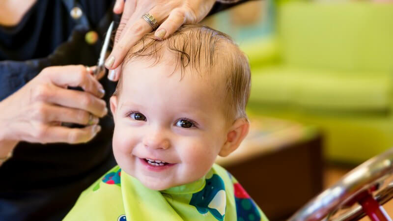 Kleiner Junge sitzt beim Friseur und bekommt seinen ersten Haarschnitt