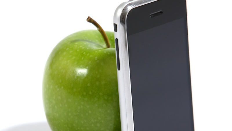 Grüner, frischer Apfel neben Rückseite eines Handys auf weißem Hintergrund