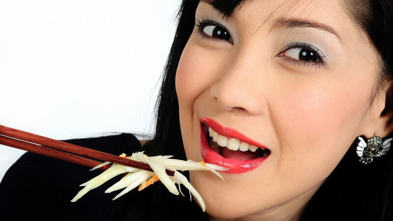 Junge asiatische Frau isst Salat mit Stäbchen