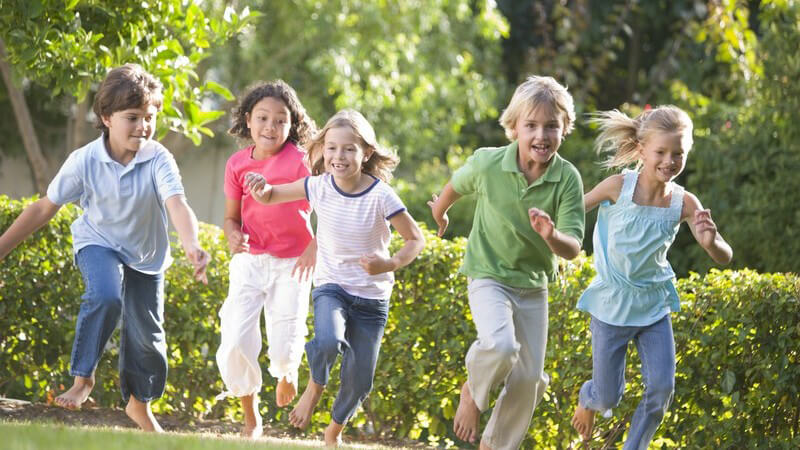 Fünf kleine Kinder laufen barfuß über eine Wiese