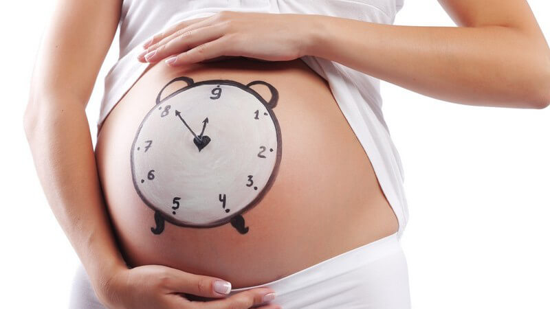 Schwangere zeigt Babybauch in Kamera, darauf ist Uhr gemalt, Geburtstermin
