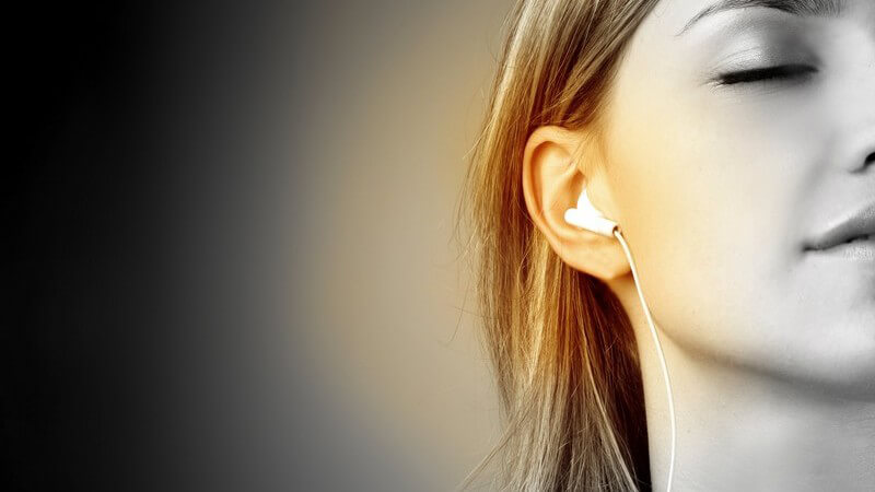 Schwarz-weiß Bild junge Frau hört über Kopfhörer Musik, Ohr ist gelb beleuchtet