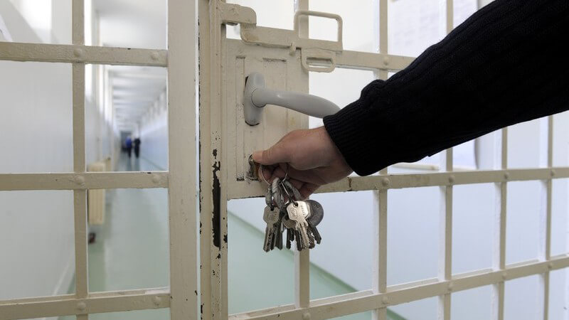 Wärter mit Schlüssel im Schloss einer weißen Gefängnistür