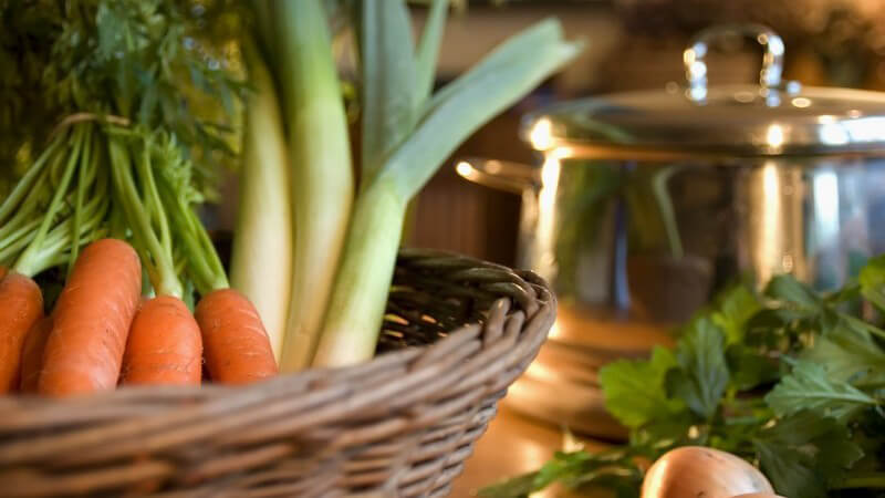 Frisches Gemüse im Korb auf Tisch, daneben Kochtopf