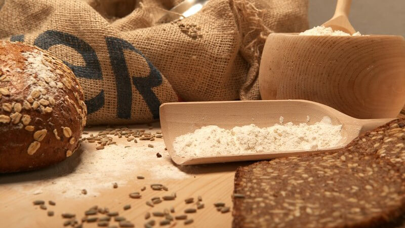 Säcke mit Getreide, Brot, teils geschnitten, Mehl auf Holzbrett