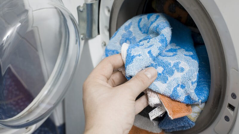 Bunte Wäsche wird in Waschmaschine gesteckt