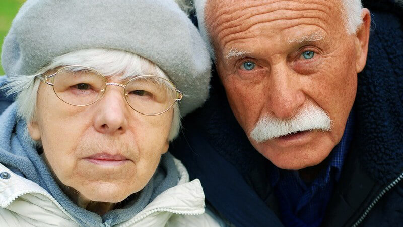 Senioren - Frau mit Brille und grauem Hut neben einem Mann mit weißem Schnurrbart