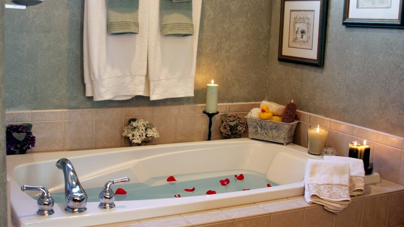 Luxus Badewanne mit Rosenblättern, umgeben von Kerzen im Badezimmer