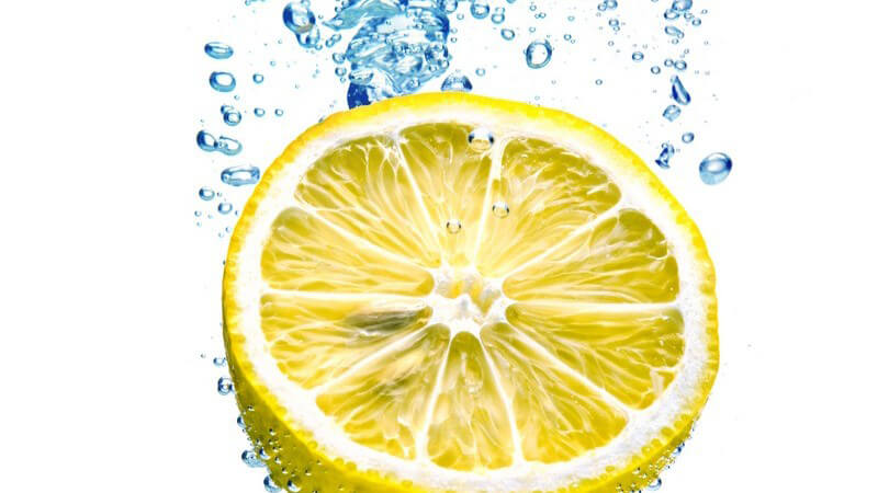Aufgeschnittene Zitrone fällt ins Wasser und hinterlässt Wasserblasen unter Oberfläche