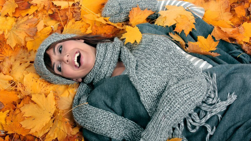 Junge Frau mit Mütze und Schal liegt auf Herbstblättern