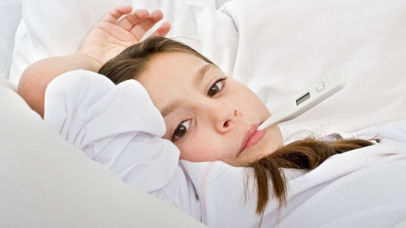 Kleines Mädchen mit Fieberthermometer im Mund liegt im Bett