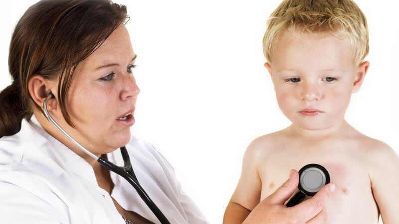 Ältere Kinderärztin links in Kittel untersucht kleinen unbekleideten blonden Jungen mit Stetoskop an der Brust