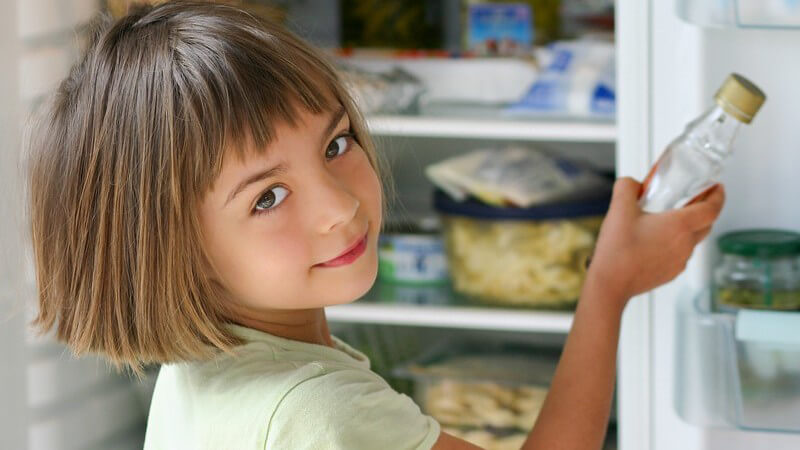 Kleines Mädchen holt Sirup aus dem Kühlschrank