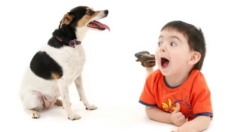 Kleiner Junge mit aufgerissenem Mund liegt auf dem Bauch neben einem Hund