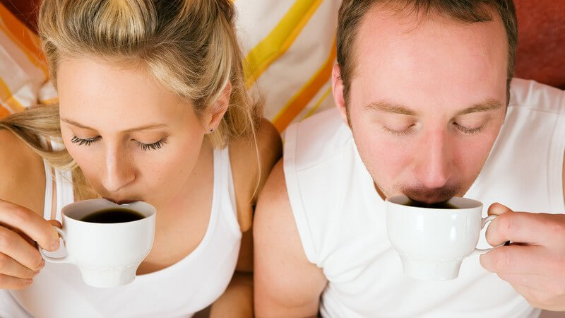 Ansicht von oben: Paar liegt im Bett und trinkt Tasse Kaffee