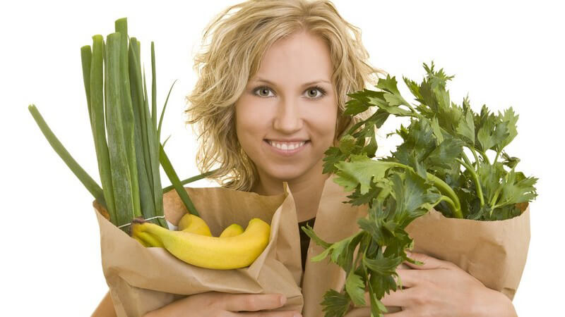 Frau hält Papiertüten mit Obst und Gemüse lachend im Arm, weißer Hintergrund