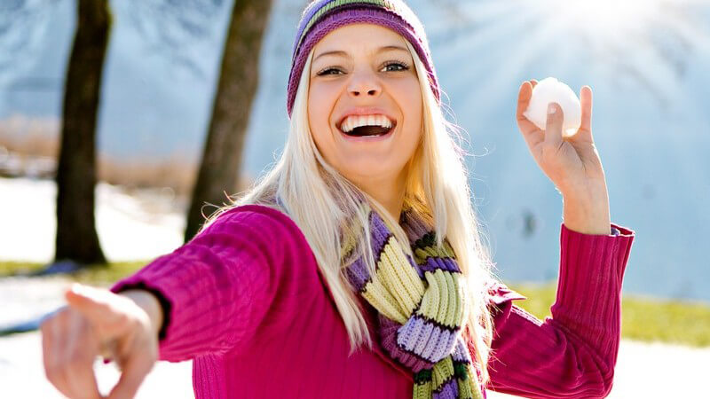 Junge Frau draußen will Schneeball auf Kamera werfen