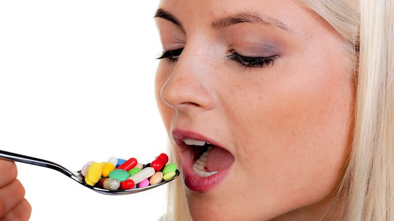 Nahaufnahme Frau mit offenem Mund hält Löffel mit bunten Pillen davor