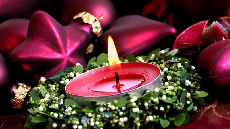 Rotes brennendes Teelicht, im Hintergrund Weihnachtskugeln