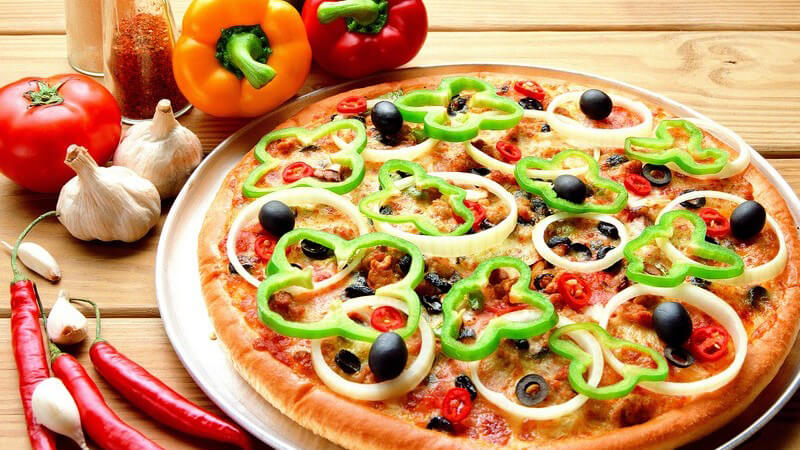Frische vegetarische Pizza, daneben Paprika, Peperoni, Tomaten, Knoblauch