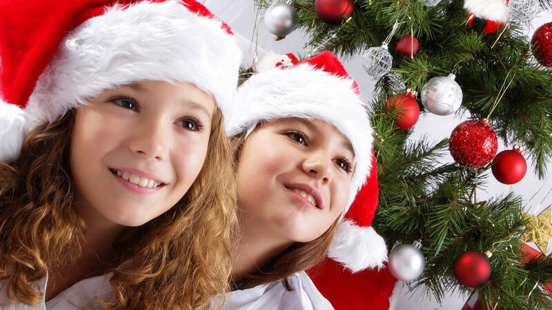 Zwei Mädchen mit Nikolausmütze vor einem geschmückten Weihnachtsbaum