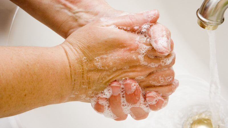Hände mit Schaum unterm Wasserhahn in weißem Waschbecken