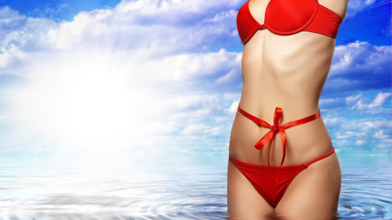 Junger Frauenkörper in rotem Bikini im Wasser, Schleife um Bauch, blauer Himmel
