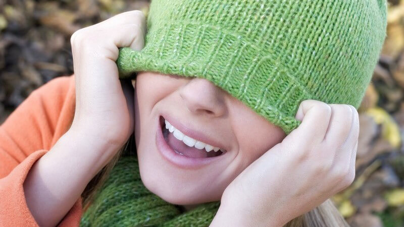 Mädchen zieht grüne Mütze bis zur Nase hinunter und lacht