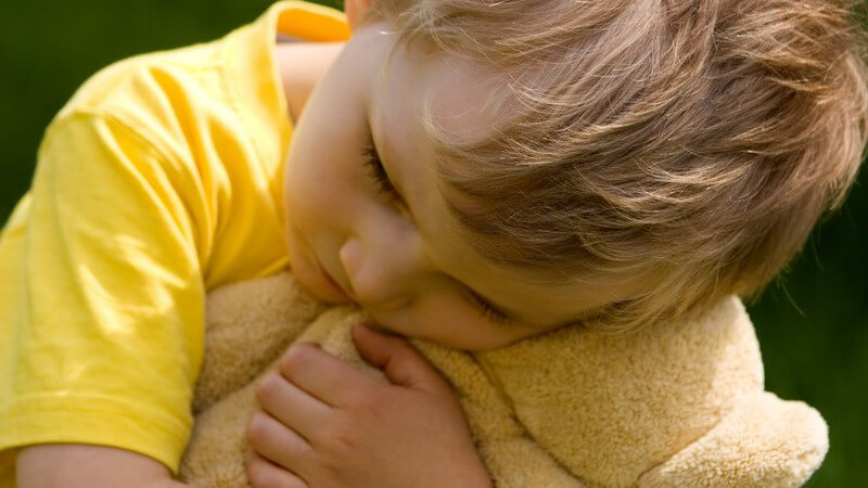 Kleiner Junge in gelbem T-Shirt knuddelt mit seinem beigefarbenen Teddy