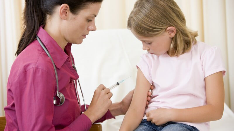 Impfung - Junge, schwarzhaarige Ärztin in lila Bluse gibt einem Mädchen eine Injektion in den Oberarm