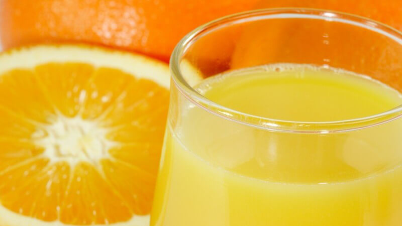 Glas Orangensaft, daneben frische halbe Orange