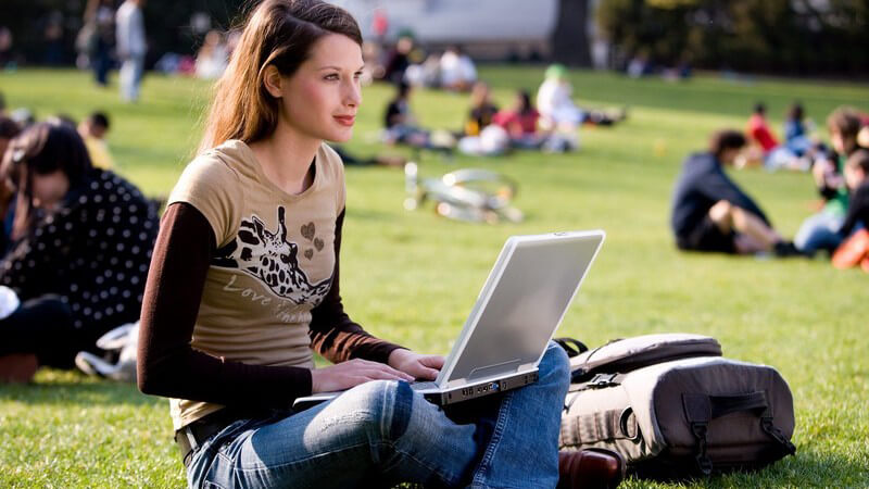 Schlanke Frau im Schneidersitz mit Laptop im Park