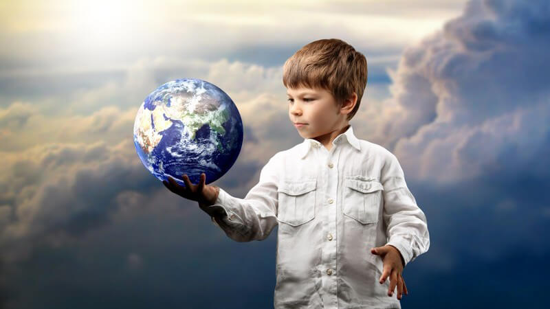 Kleiner Junge mit Globus in der Hand, dahinter Himmel über den Wolken