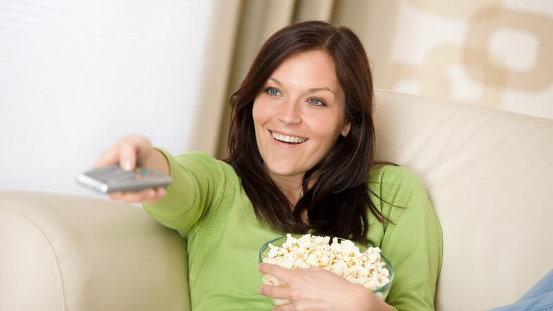 Junge Frau mit Popcorn auf Couch, schaut Fernsehen