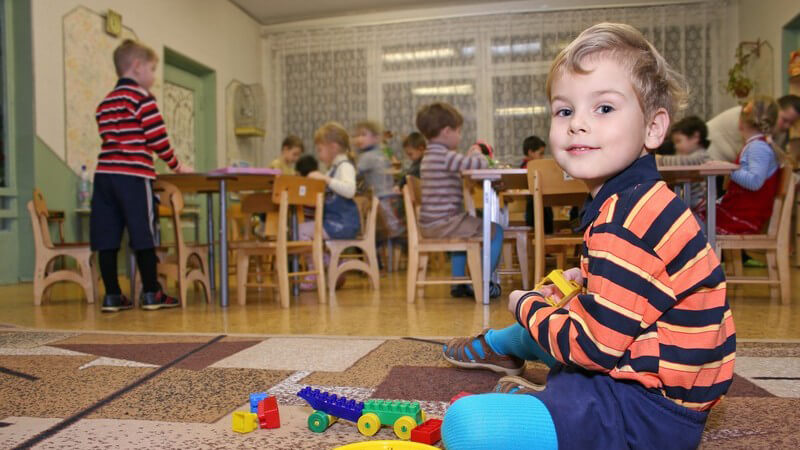 Kindergarten, Junge sitzt auf Teppich und spielt