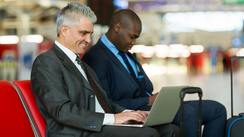 Geschäftsreise - zwei Männer mit Laptop warten im Gate eines Flughafens