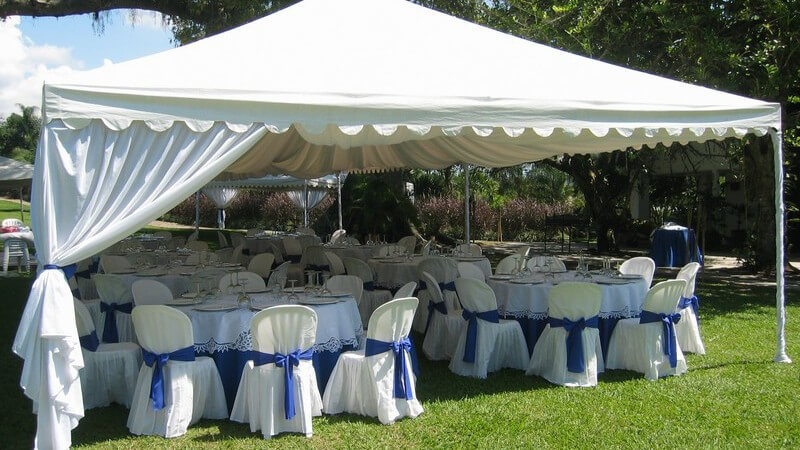Gedeckte Tische unter weißem Zelt im Garten für Hochzeitsfeier