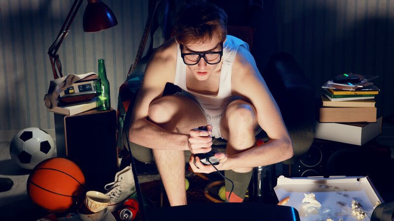 Nerd in Unterwäsche sitzt nachts in seinem Chaos-Zimmer und spielt Videospiele