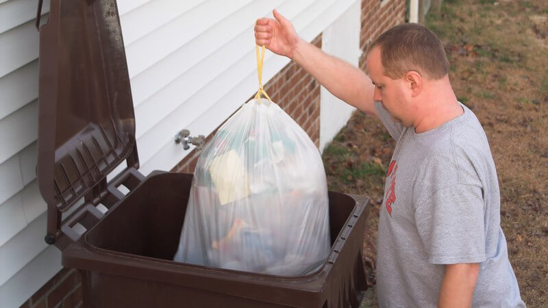 Mann wirft Müllbeutel in große Mülltonne im Garten oder Hof