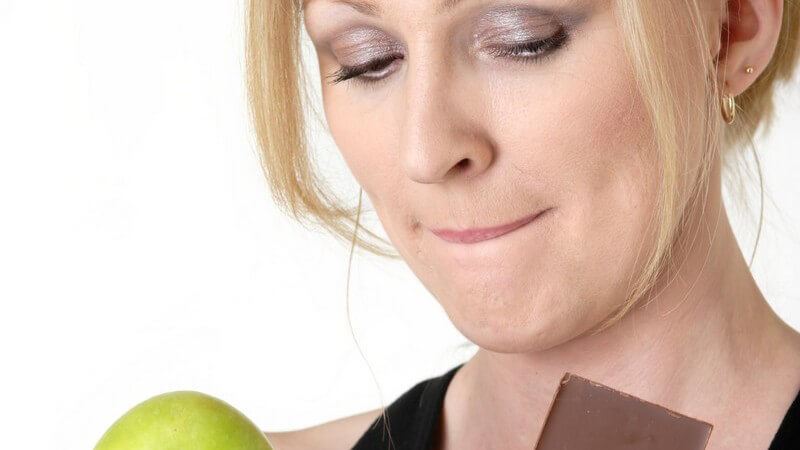 Frau hält Apfel und Schokolade in Händen, muss sich entscheiden