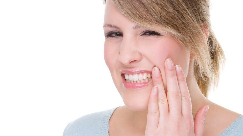 Frau mit Zahnschmerzen hält sich Hand an Wange