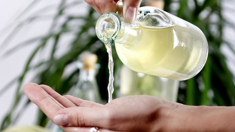 Massage - Grünes Massageöl fließt aus einer Flasche in die aufgehaltene Hand