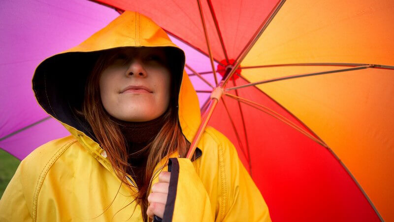 Junge Frau in gelbem Regenmantel unter buntem Regenschirm