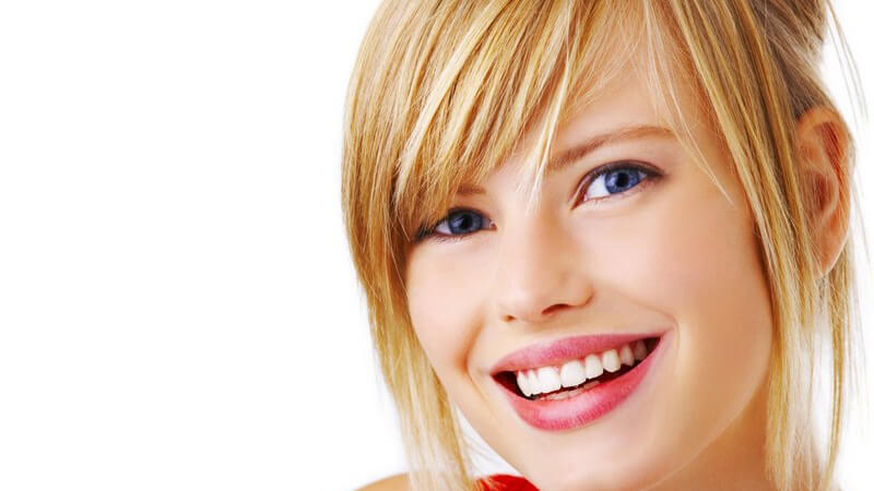 Gesicht Junges blondes Mädchen mit Pony und Fransenschnitt, blaue Augen, lächelt, rotes Top, gerade Zähne