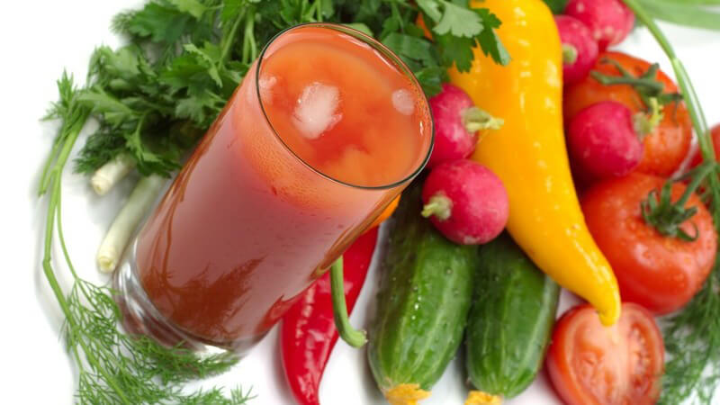 Glas mit Tomatensaft und Eiswürfeln, daneben frisches Gemüse