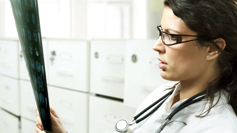 Brünette Ärztin mit Brille und Stethoskop analysiert ein Röntgenbild in ihren Händen