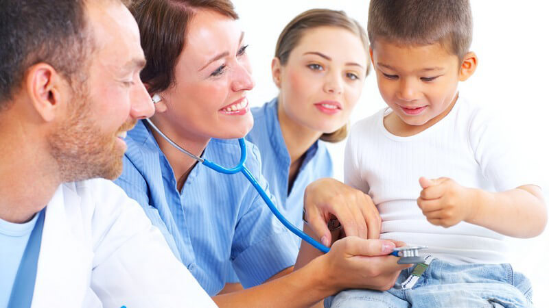 Gesundheitsvorsorge, ein Arzt und zwei Krankenschwestern behandeln kleinen Jungen, mit Stetoskop, lächelnd, heller Raum