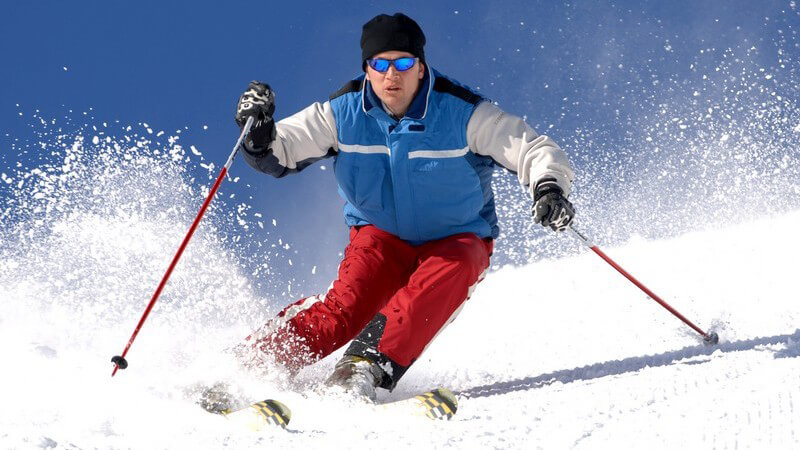 Skifahrer mit roter Hose und roten Stöcken bei einer schwungvollen Abfahrt